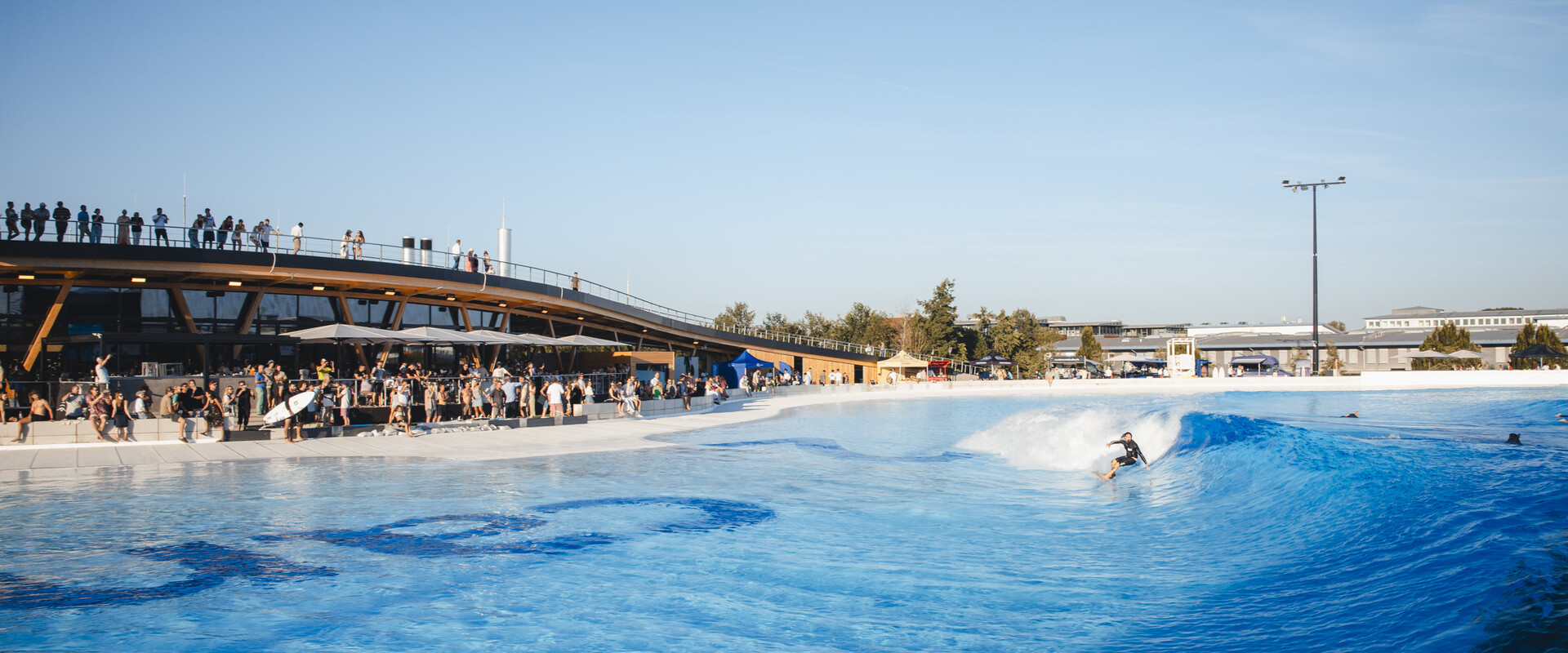 Surfer:innen im Wavepool des Surfparks bei M&uuml;nchen, die gemeinsam perfekte Wellen reiten &ndash; Surfen f&uuml;r alle Levels.