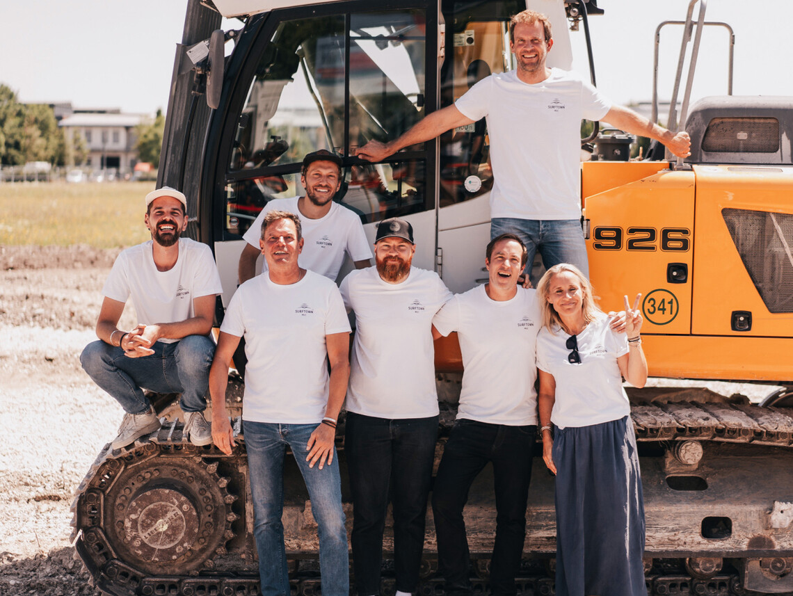 The o2 SURFTOWN MUC team stands in front of an excavator.